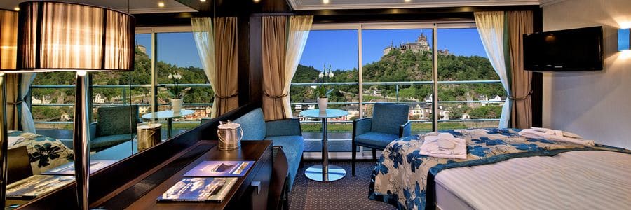 Avalon Waterways Panorama Suite with floor-to-ceiling windows overlooking a European river valley and castle scenery.