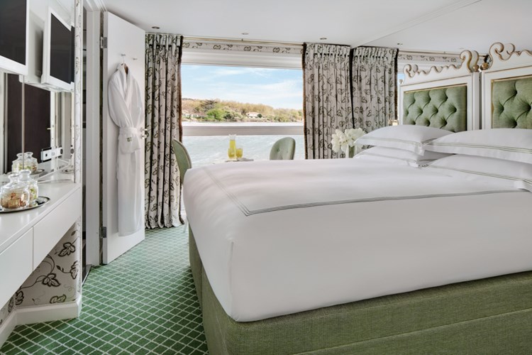 Luxury Uniworld river cruise stateroom with plush bed, elegant décor, and large window overlooking the river.