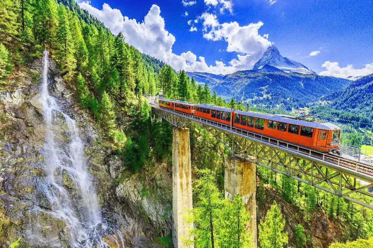 Best way to see Europe without rushing by train through scenic mountains with a waterfall and panoramic views