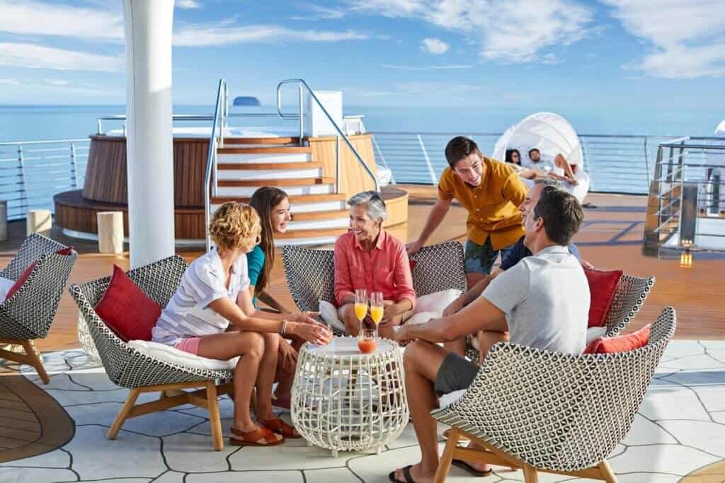 Multigenerational group relaxing together on a cruise ship deck with ocean views and drinks, enjoying a Caribbean group cruise