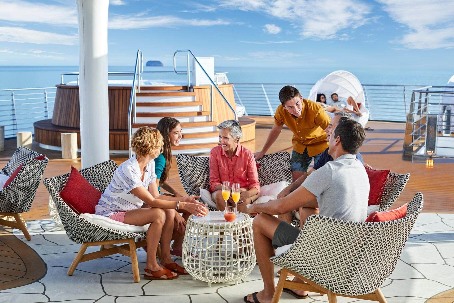 Multigenerational group relaxing together on a cruise ship deck with ocean views and drinks, enjoying a Caribbean group cruise
