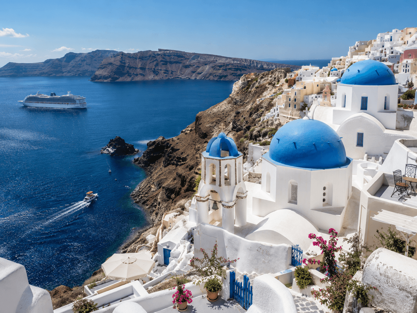 Blue-domed churches and white buildings overlooking the Santorini caldera with a cruise ship tendering in the bay below