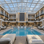 The Haven Courtyard pool on Norwegian Encore under its retractable glass roof, with loungers around the water